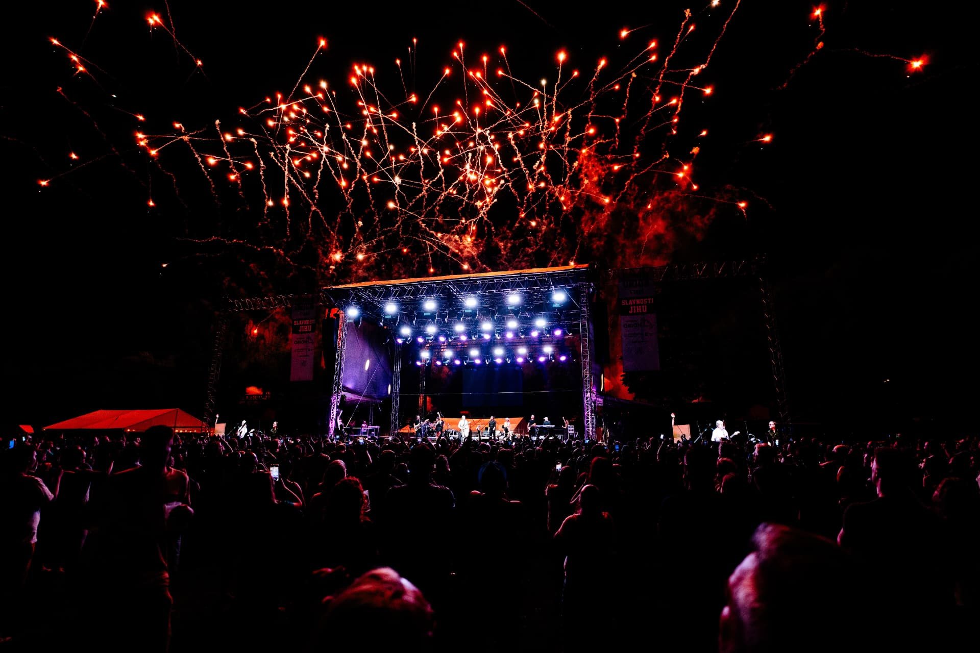 Široký noční pohled z publika na hlavní pódium festivalu Slavnosti Jihu s ohňostrojem nad stage a davem návštěvníků