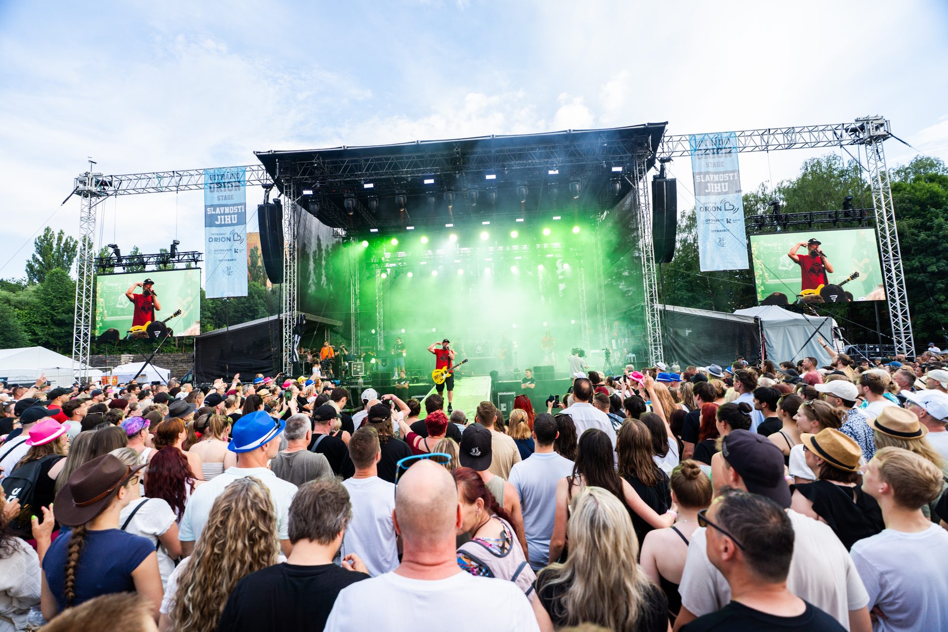 Široký pohled z publika na hlavní pódium Orion Stage festivalu Slavnosti Jihu s technickou produkcí a davem návštěvníků